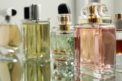 Photo of Different aromatic perfumes in bottles on mirror surface, closeup