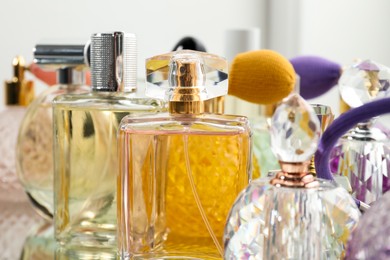 Photo of Different aromatic perfumes in bottles on mirror surface, closeup