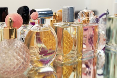 Photo of Different aromatic perfumes in bottles on mirror surface, closeup