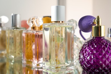 Different aromatic perfumes in bottles on mirror surface, closeup