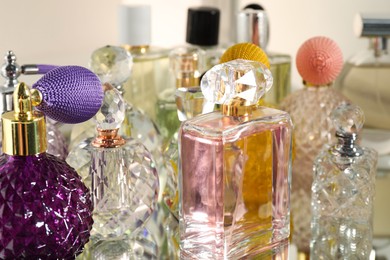 Photo of Different aromatic perfumes in bottles on mirror surface, closeup