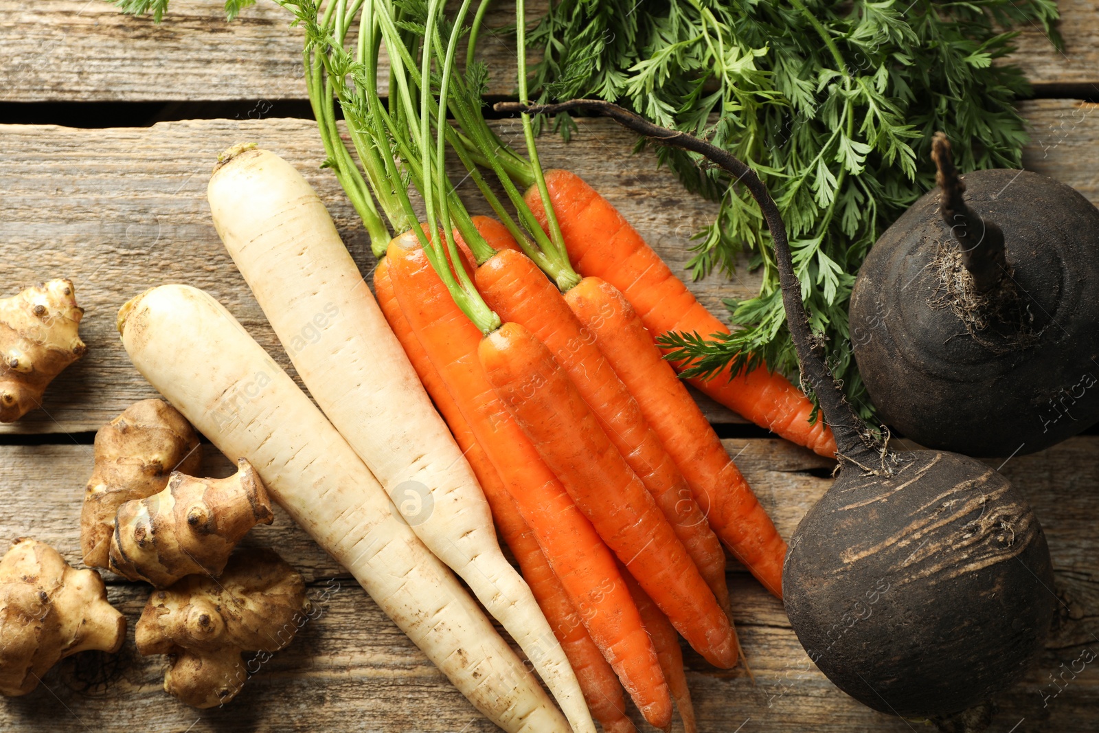 Photo of Different root vegetables on wooden table, flat lay