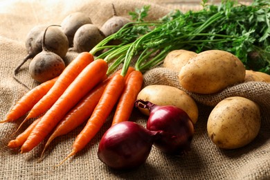 Photo of Different root vegetables on burlap fabric, closeup