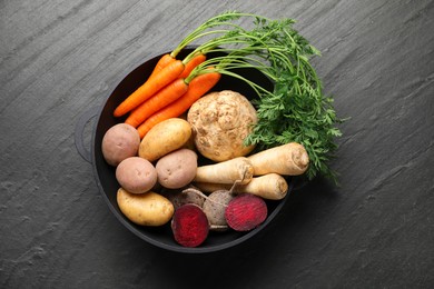 Photo of Different root vegetables in pot on black table, top view