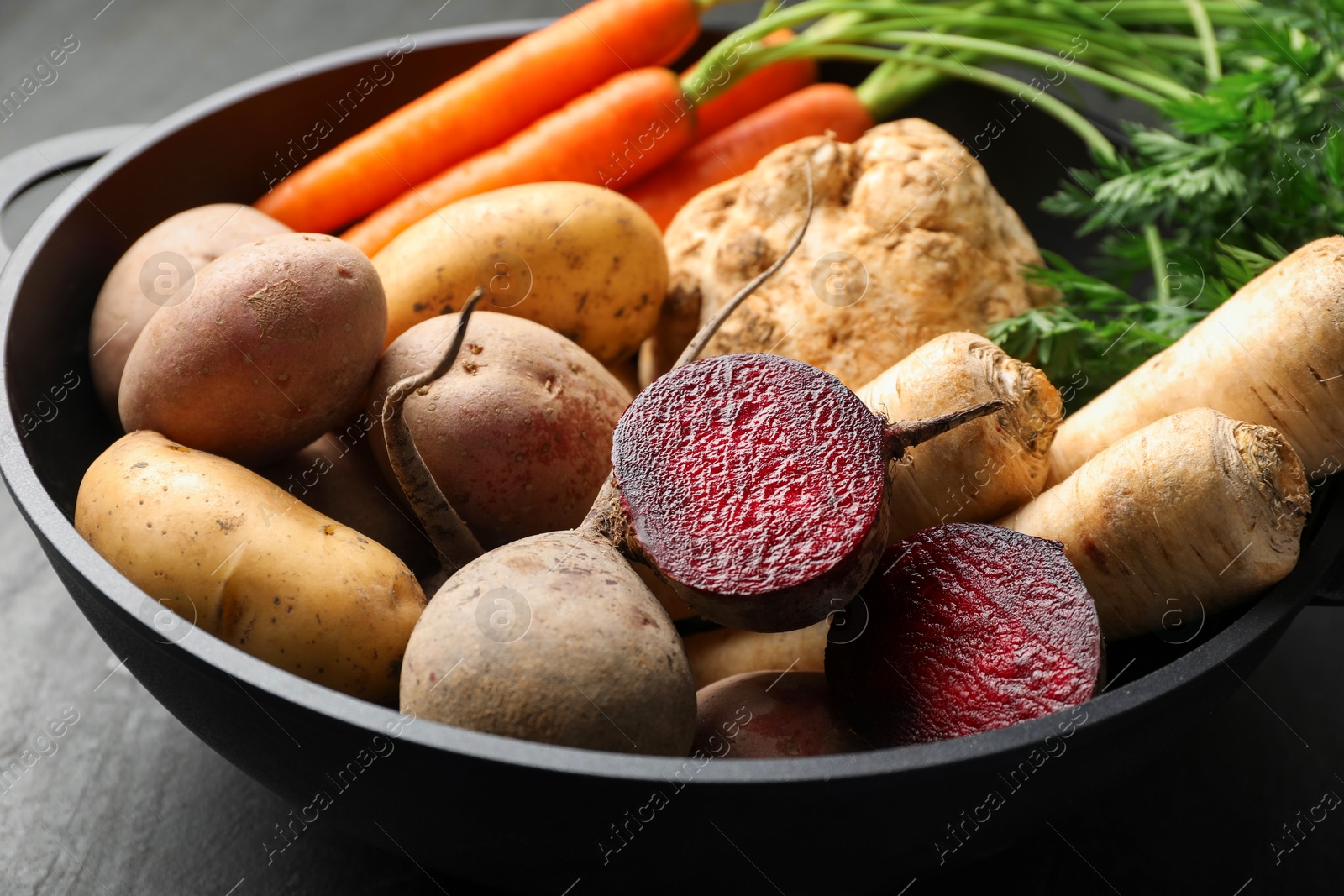 Photo of Different root vegetables in pot on black table, closeup