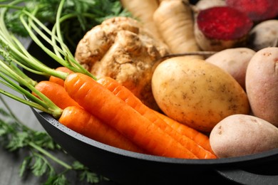 Photo of Different root vegetables in pot on black table, closeup