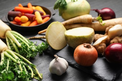 Photo of Different raw root vegetables on black table, closeup