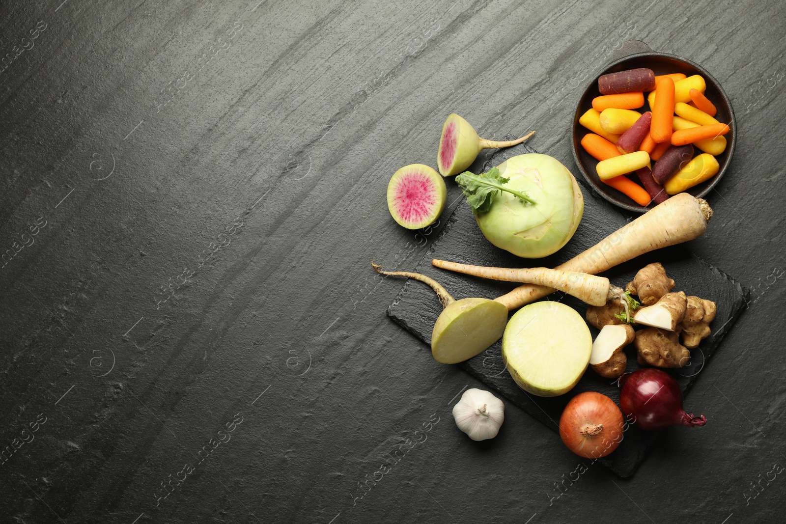 Photo of Different raw root vegetables on black table, flat lay. Space for text