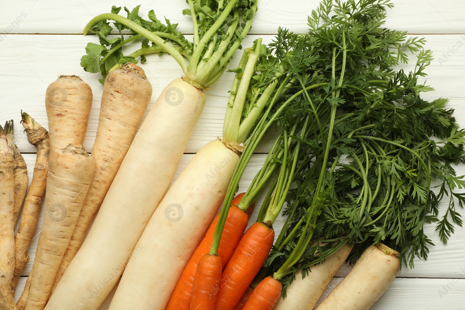 Photo of Different root vegetables on white wooden table, flat lay