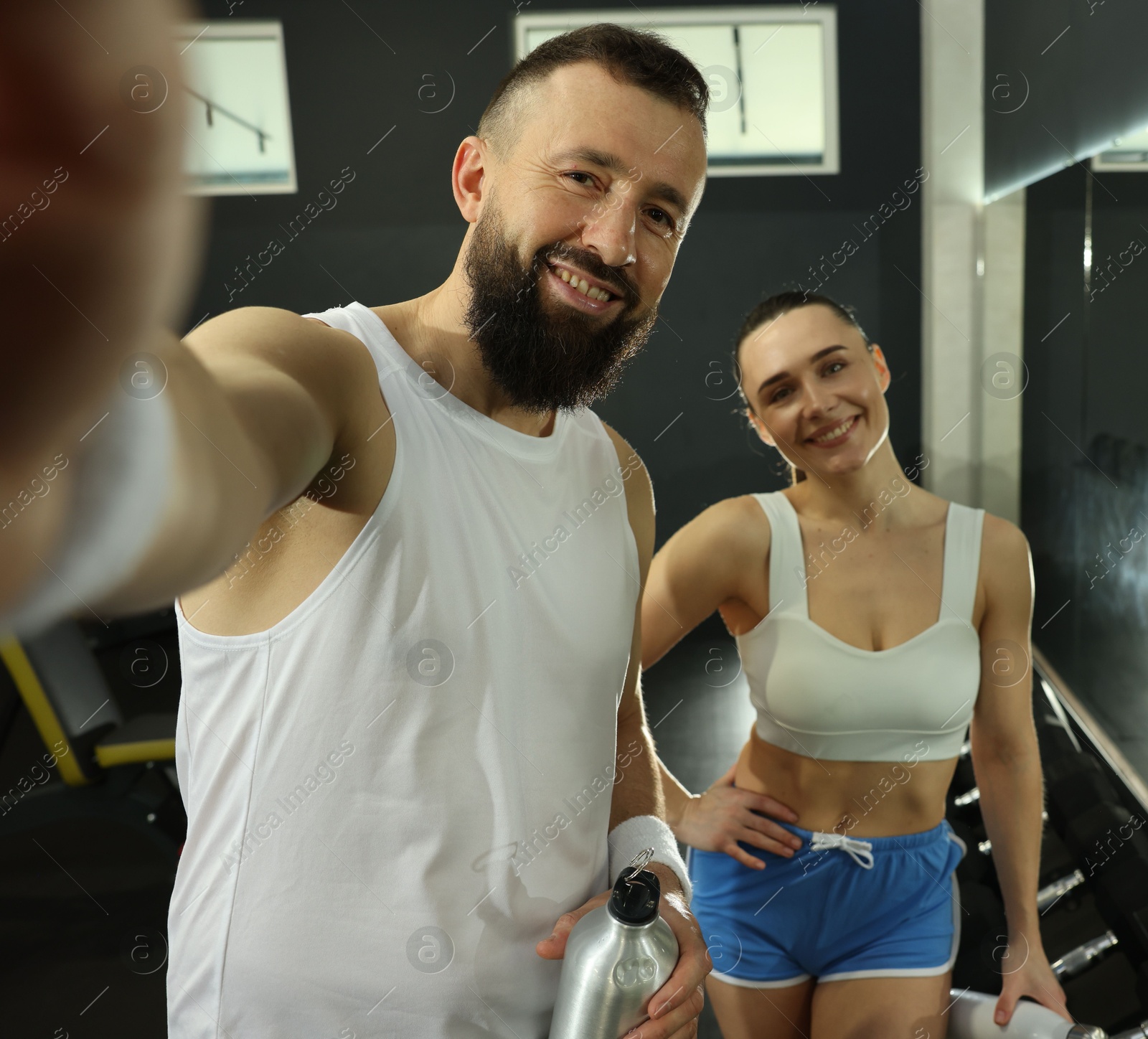 Photo of Couple with water bottles taking selfie after training in gym