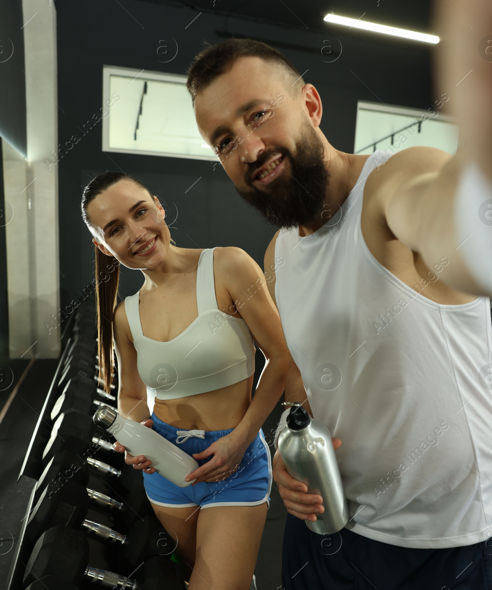 Photo of Couple with water bottles taking selfie after training in gym