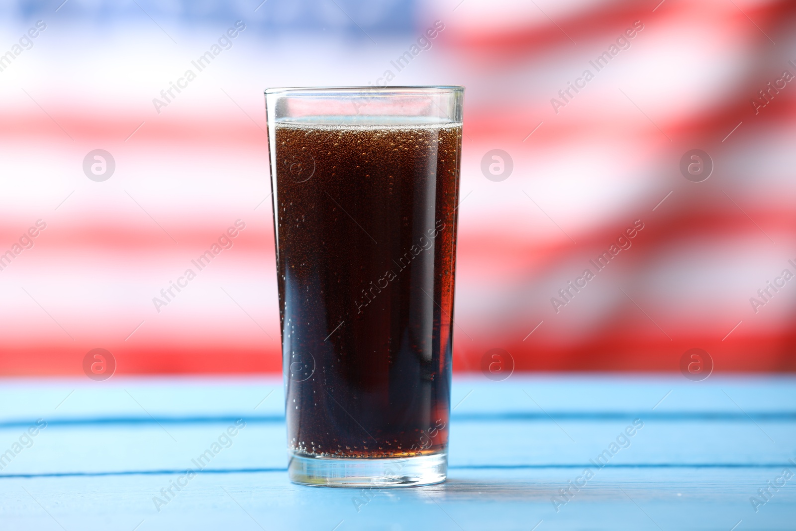 Glass of soda drink on blue wooden table against American flag, closeup Photo of Glass of soda drink on blue wooden table against American flag, closeup