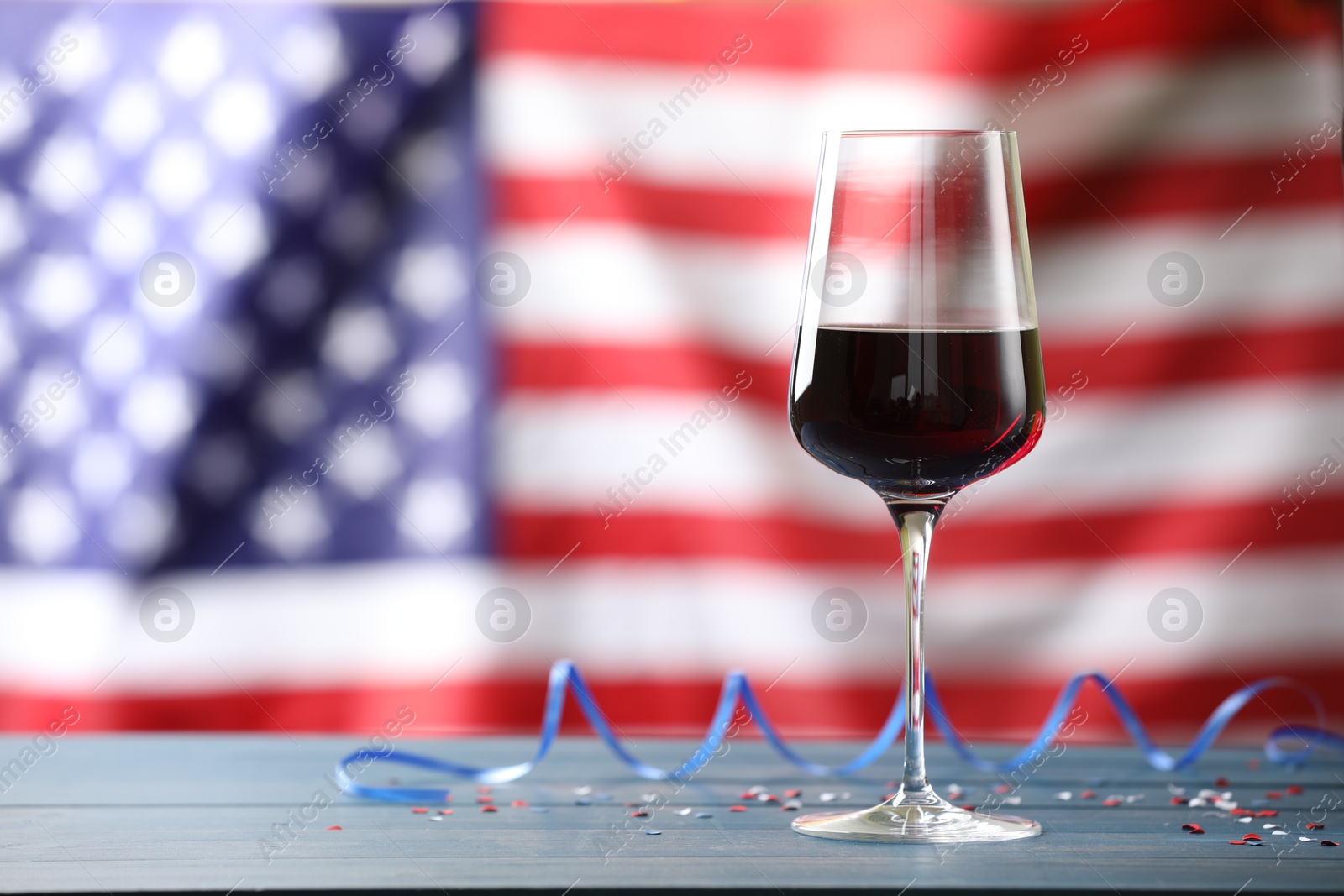 Glass of wine and party streamers on blue wooden table against American flag. Space for text Photo of Glass of wine and party streamers on blue wooden table against American flag. Space for text
