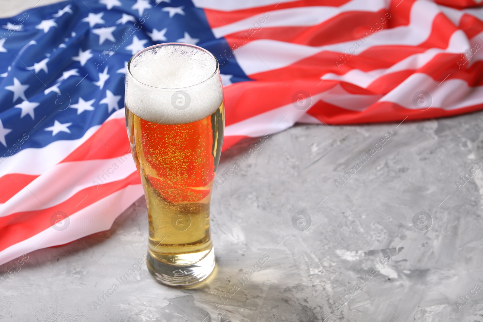 Glass of beer and American flag on grey table. Space for text Photo of Glass of beer and American flag on grey table. Space for text