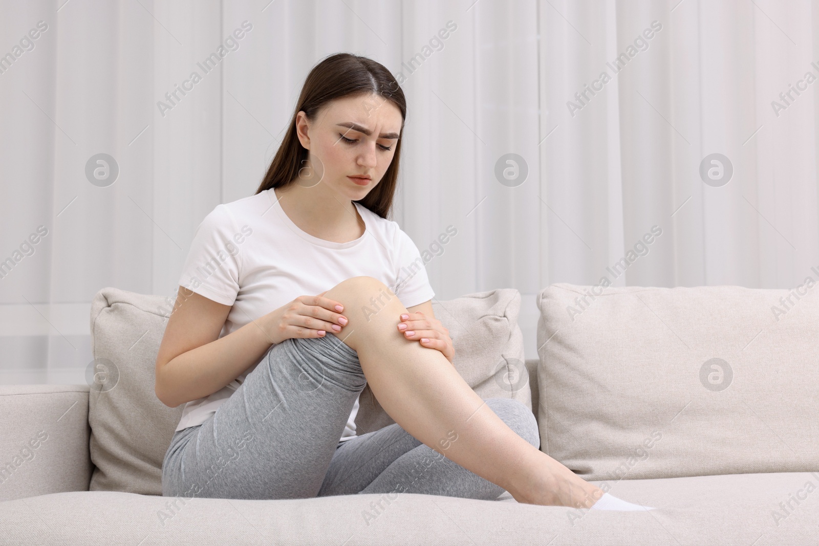 Photo of Young woman suffering from pain in knee on sofa at home. Space for text