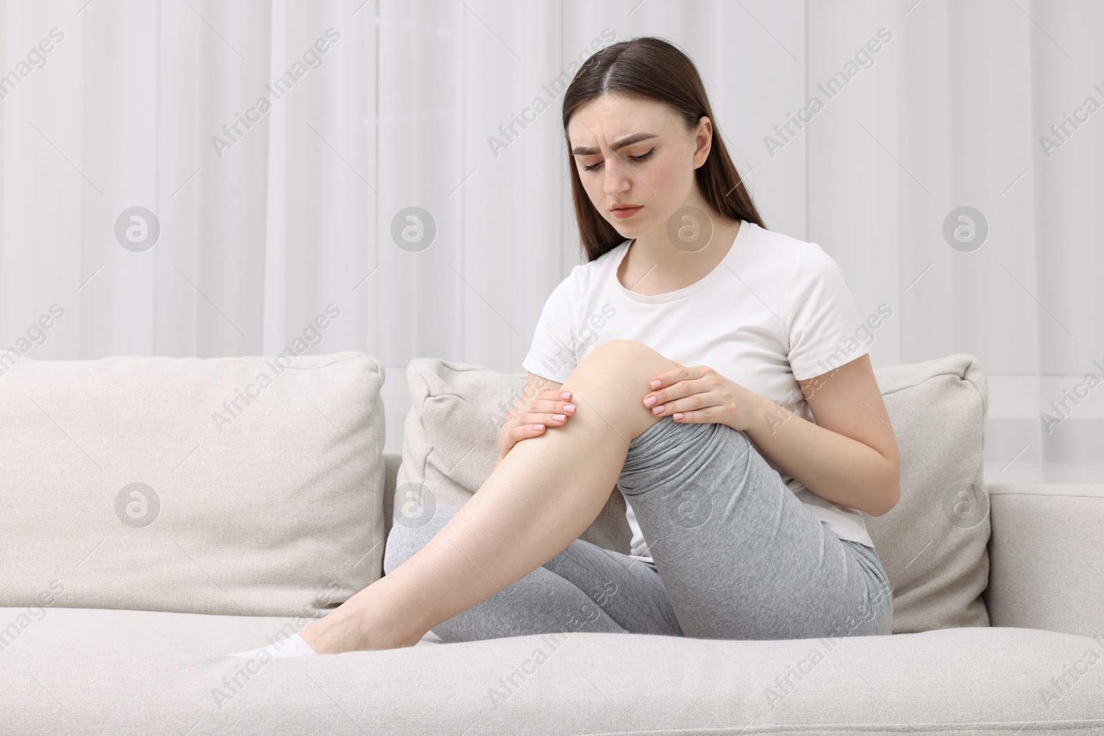 Photo of Young woman suffering from pain in knee on sofa at home. Space for text