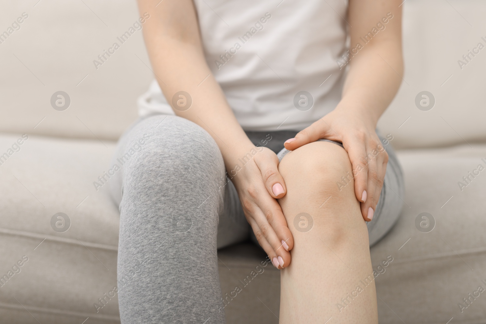 Photo of Young woman suffering from pain in knee on sofa at home, closeup