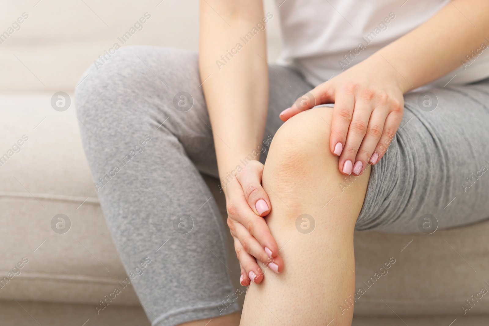 Photo of Young woman suffering from pain in knee on sofa at home, closeup