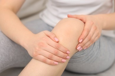 Photo of Young woman suffering from pain in knee on sofa at home, closeup