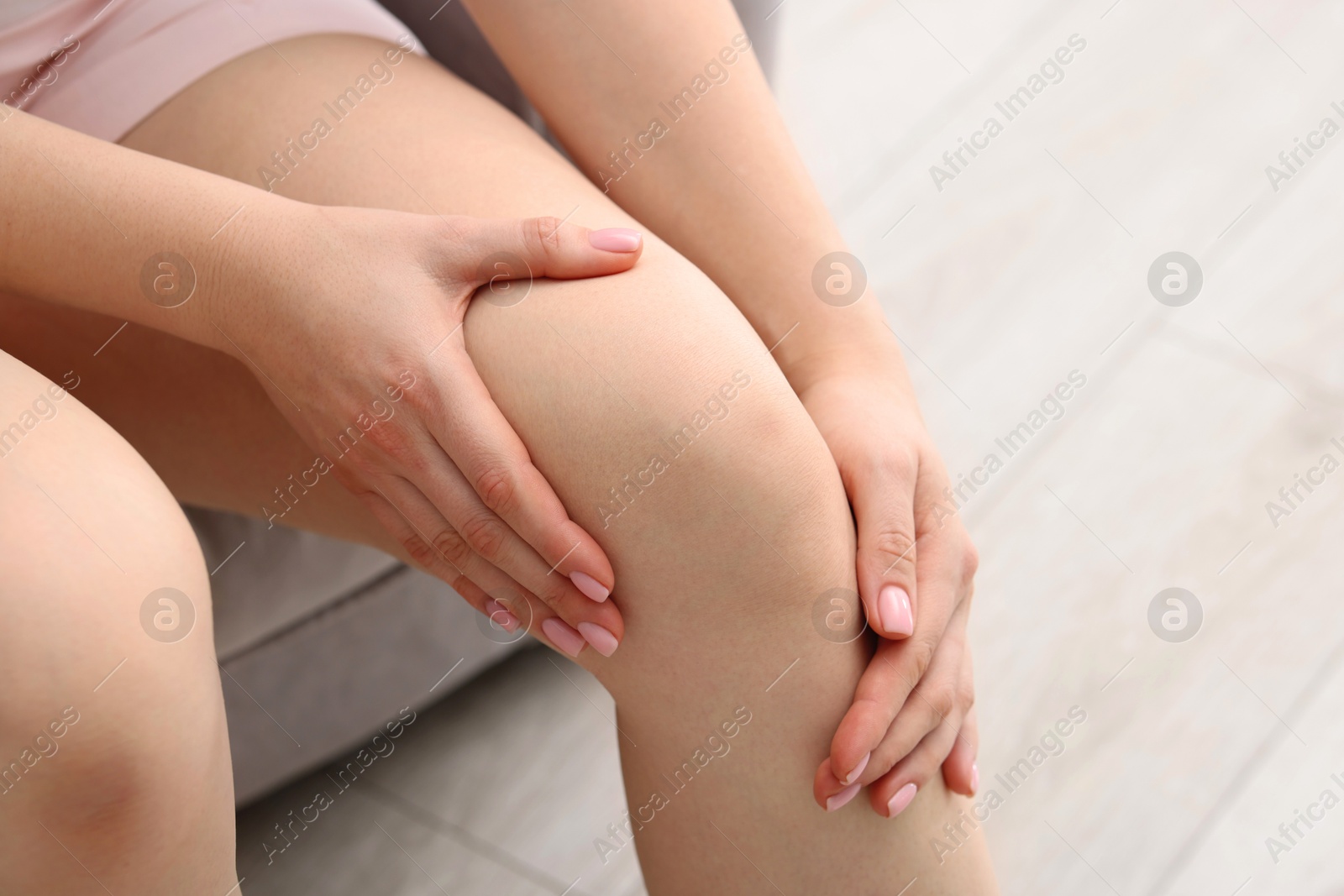 Photo of Young woman suffering from pain in knee on sofa at home, closeup