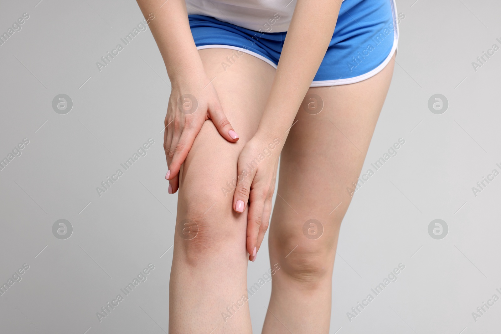 Photo of Young woman suffering from pain in knee on light grey background, closeup