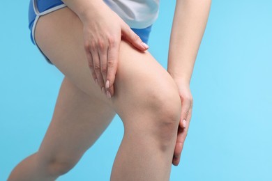 Young woman suffering from pain in knee on light blue background, closeup