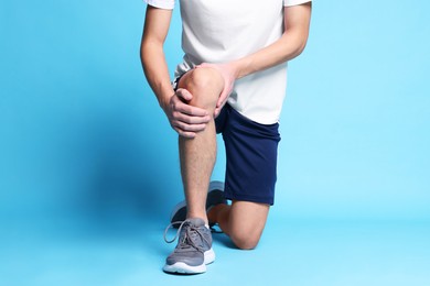 Photo of Young man suffering from pain in knee on light blue background, closeup