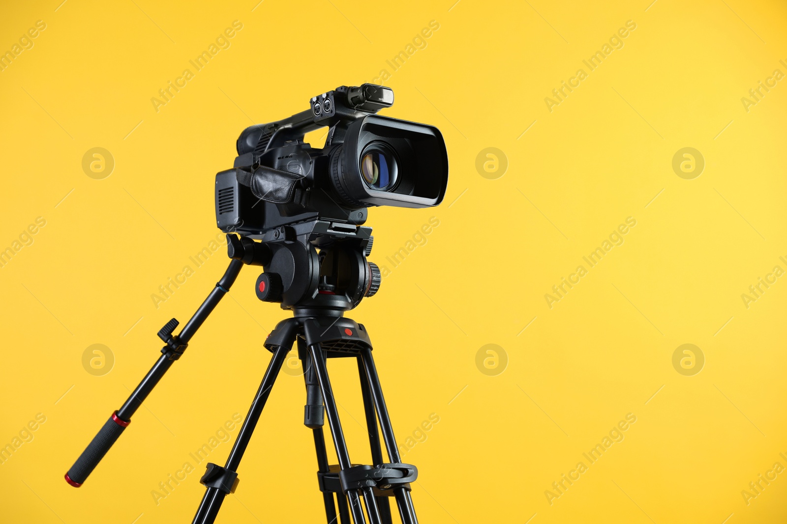 Photo of Modern video camera with tripod on yellow background, space for text