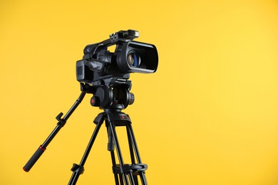 Photo of Modern video camera with tripod on yellow background, space for text