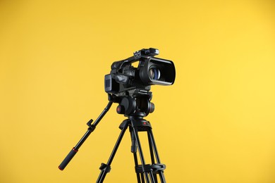 Modern video camera with tripod on yellow background