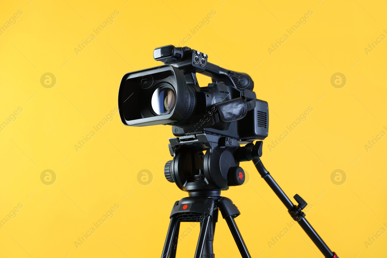 Photo of Modern video camera with tripod on yellow background, space for text