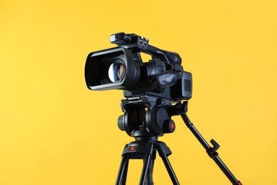 Photo of Modern video camera with tripod on yellow background, space for text