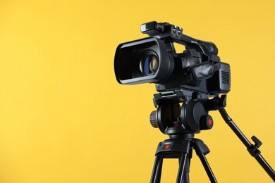 Photo of Modern video camera with tripod on yellow background, space for text