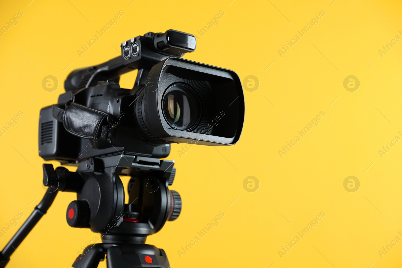 Photo of Modern video camera on yellow background, closeup. Space for text