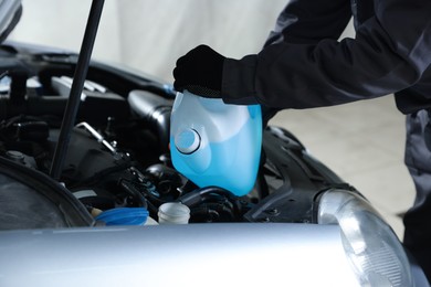 Photo of Man pouring windshield washer from plastic canister into car reservoir outdoors, closeup