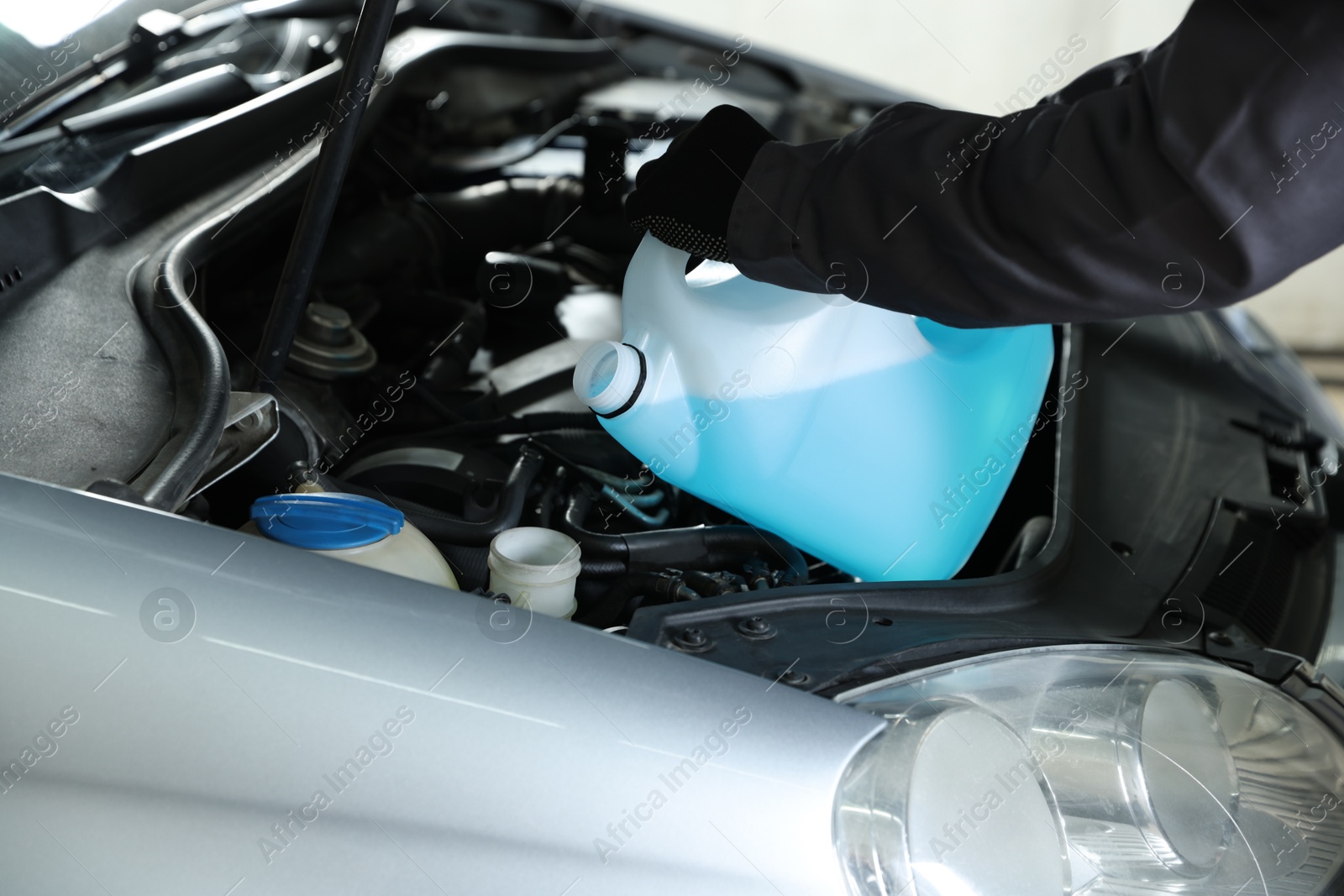 Photo of Man pouring windshield washer from plastic canister into car reservoir, closeup