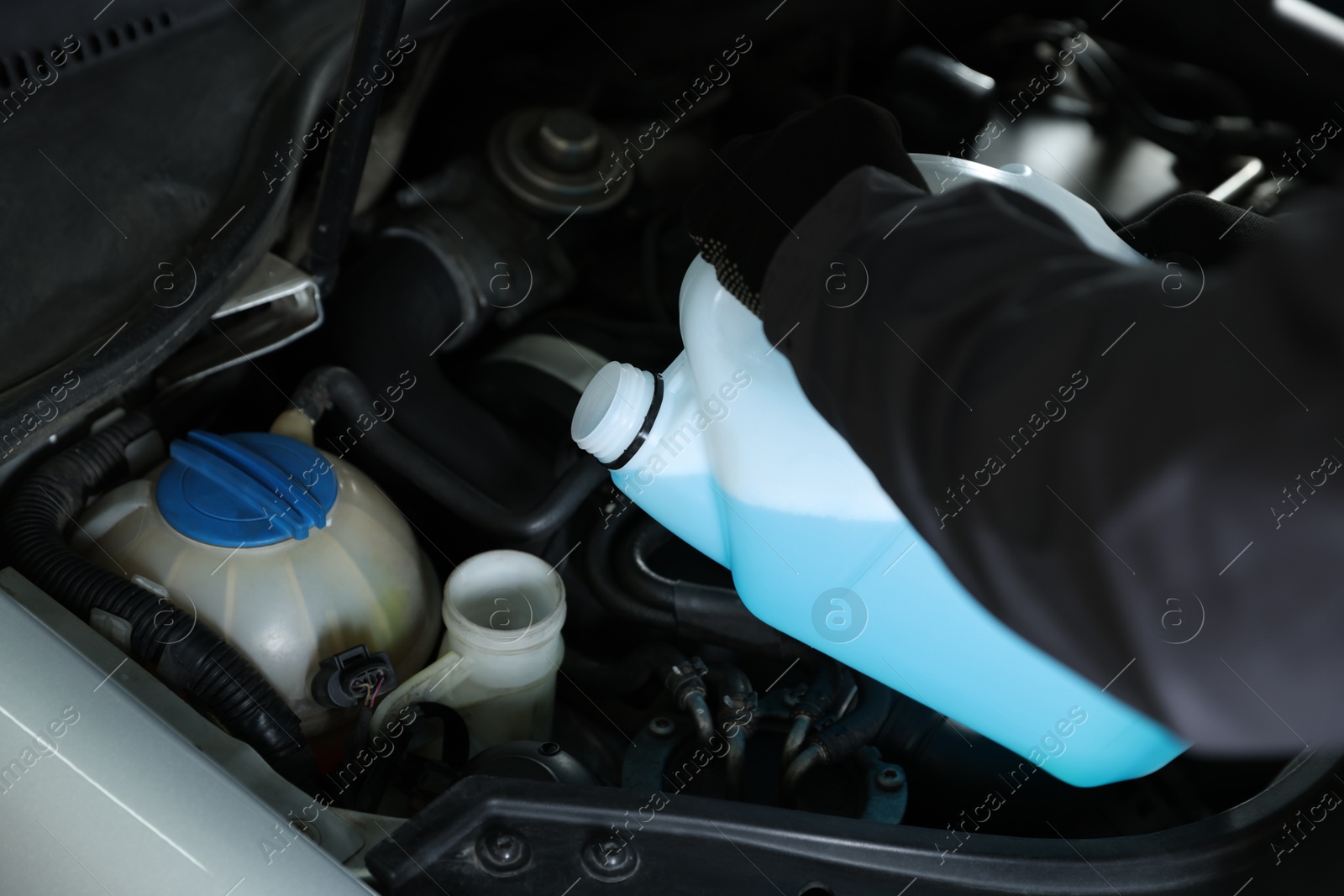 Photo of Man pouring windshield washer from plastic canister into car reservoir, closeup