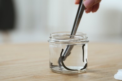 Photo of Woman taking leech from jar with tweezers on wooden table, closeup