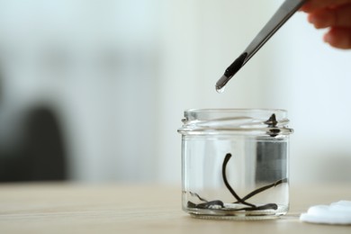 Photo of Woman taking medicinal leech from jar with tweezers on wooden table, closeup. Space for text