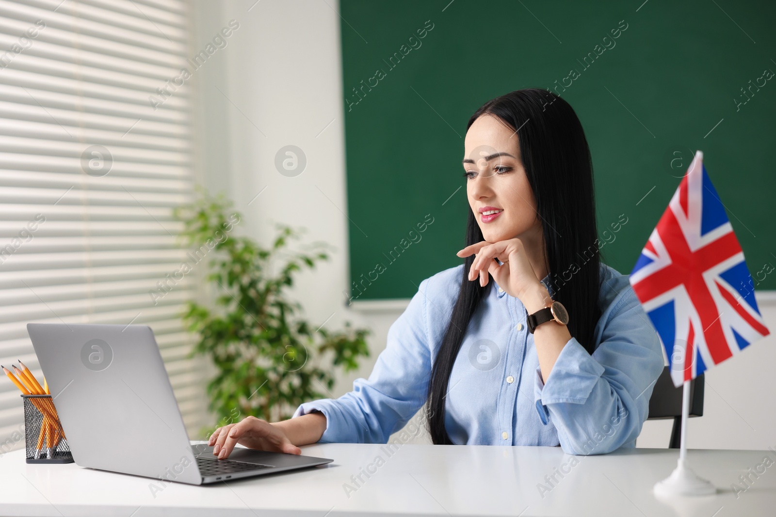 Photo of English teacher working on laptop at desk in classroom. Space for text