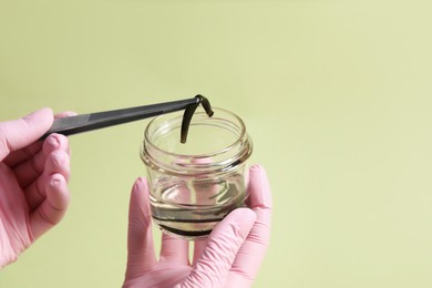 Photo of Woman taking medicinal leech from jar with tweezers on light green background, closeup. Space for text