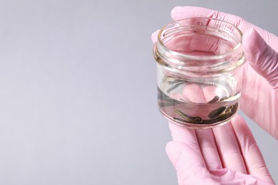 Woman holding glass jar with medicinal leeches on gray background, closeup. Space for text