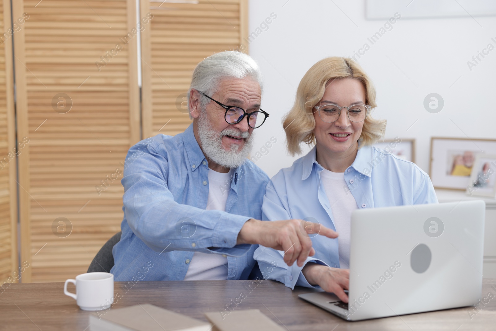 Photo of Senior man and mature woman watching something on laptop at home. Happy couple