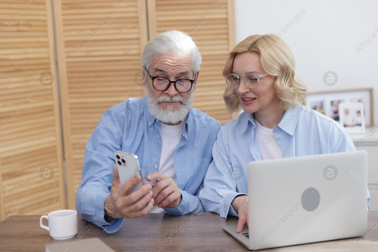 Photo of Senior man and mature woman watching something on smartphone at home. Happy couple