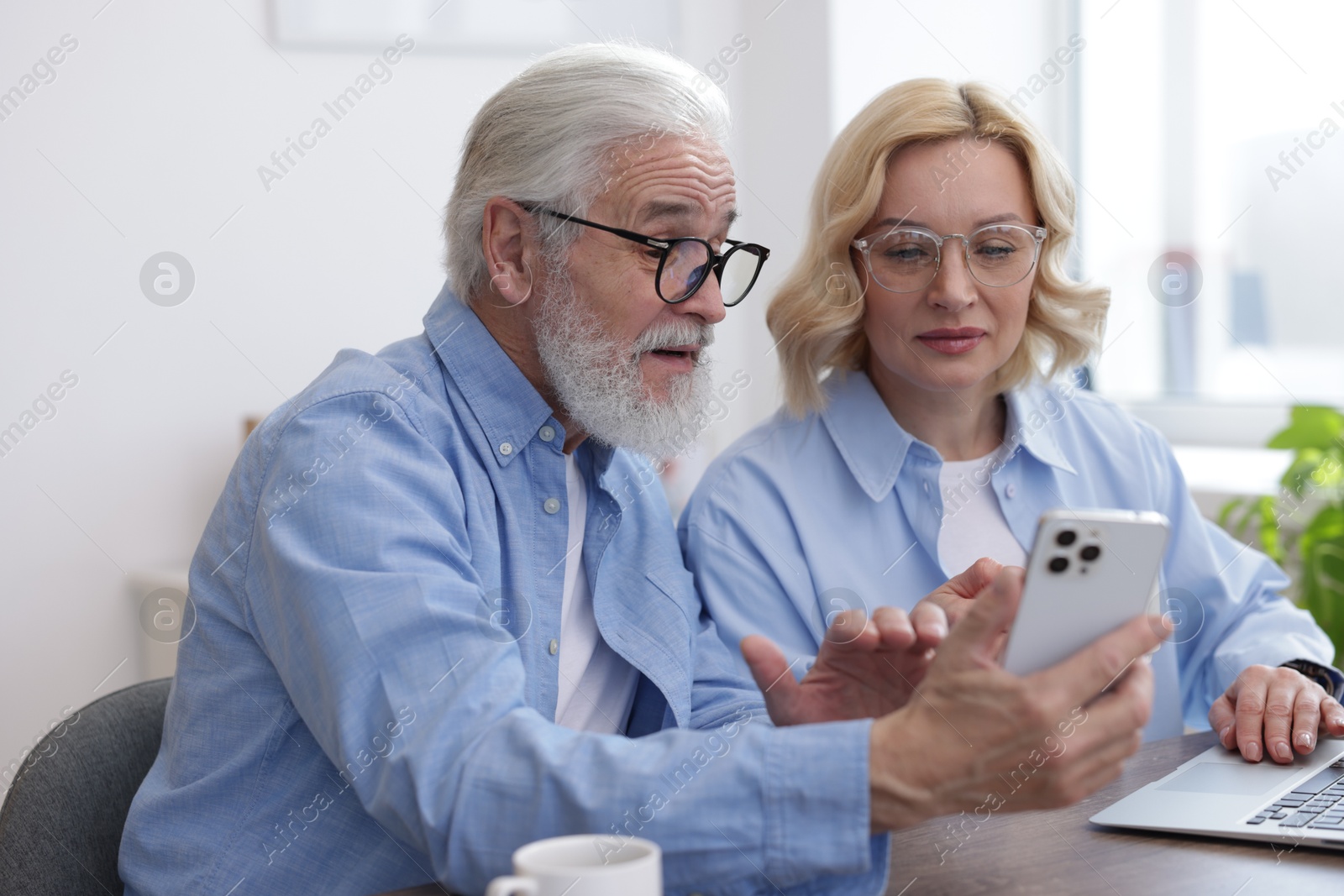 Photo of Senior man and mature woman watching something on smartphone at home. Happy couple