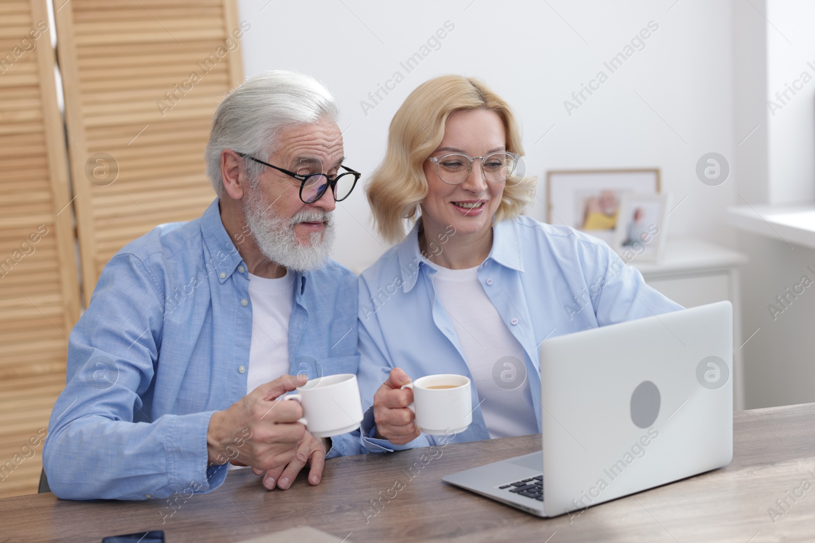 Photo of Senior man and mature woman with coffee watching something on laptop at home. Happy couple