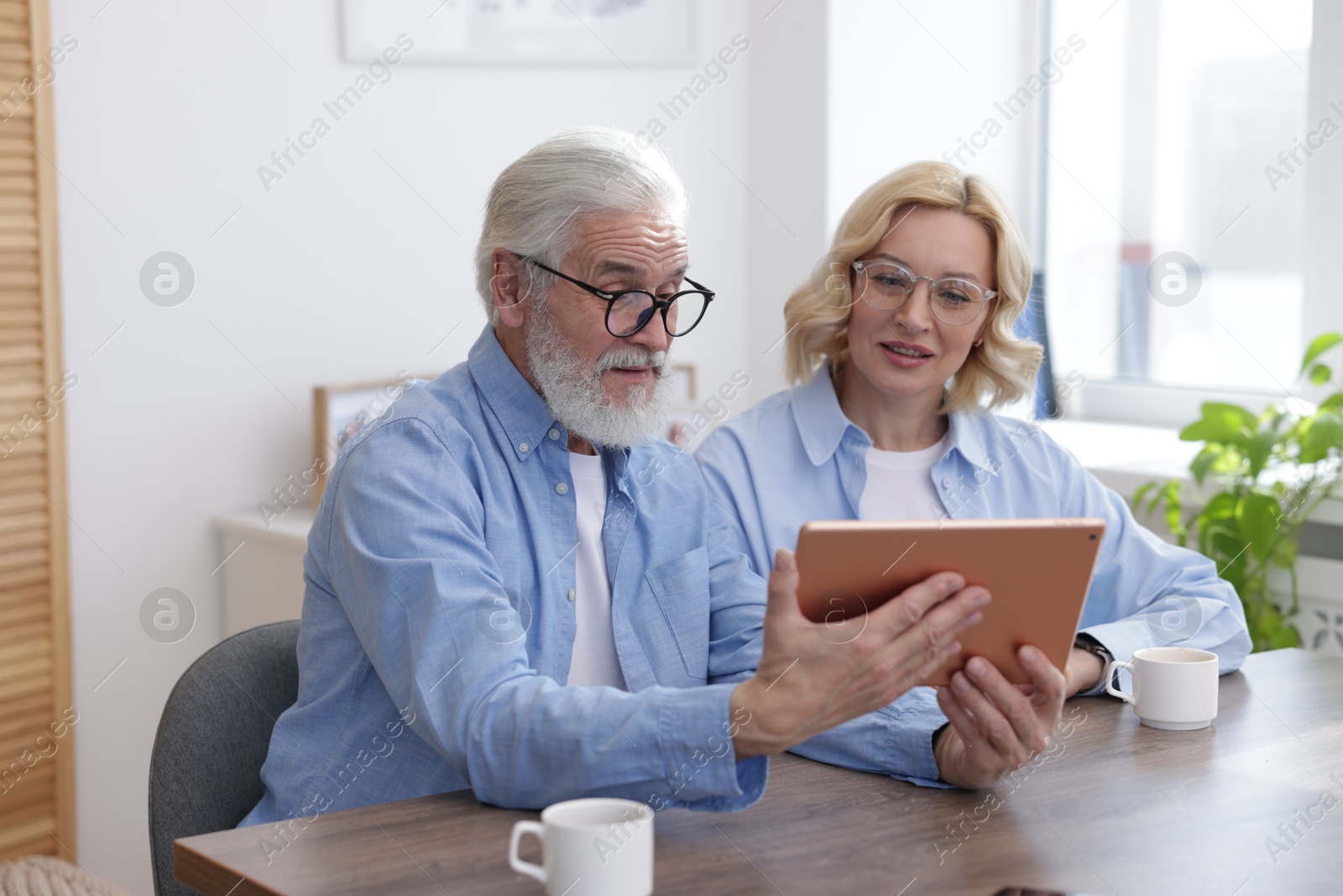 Photo of Senior man and mature woman watching something on tablet at home. Happy couple