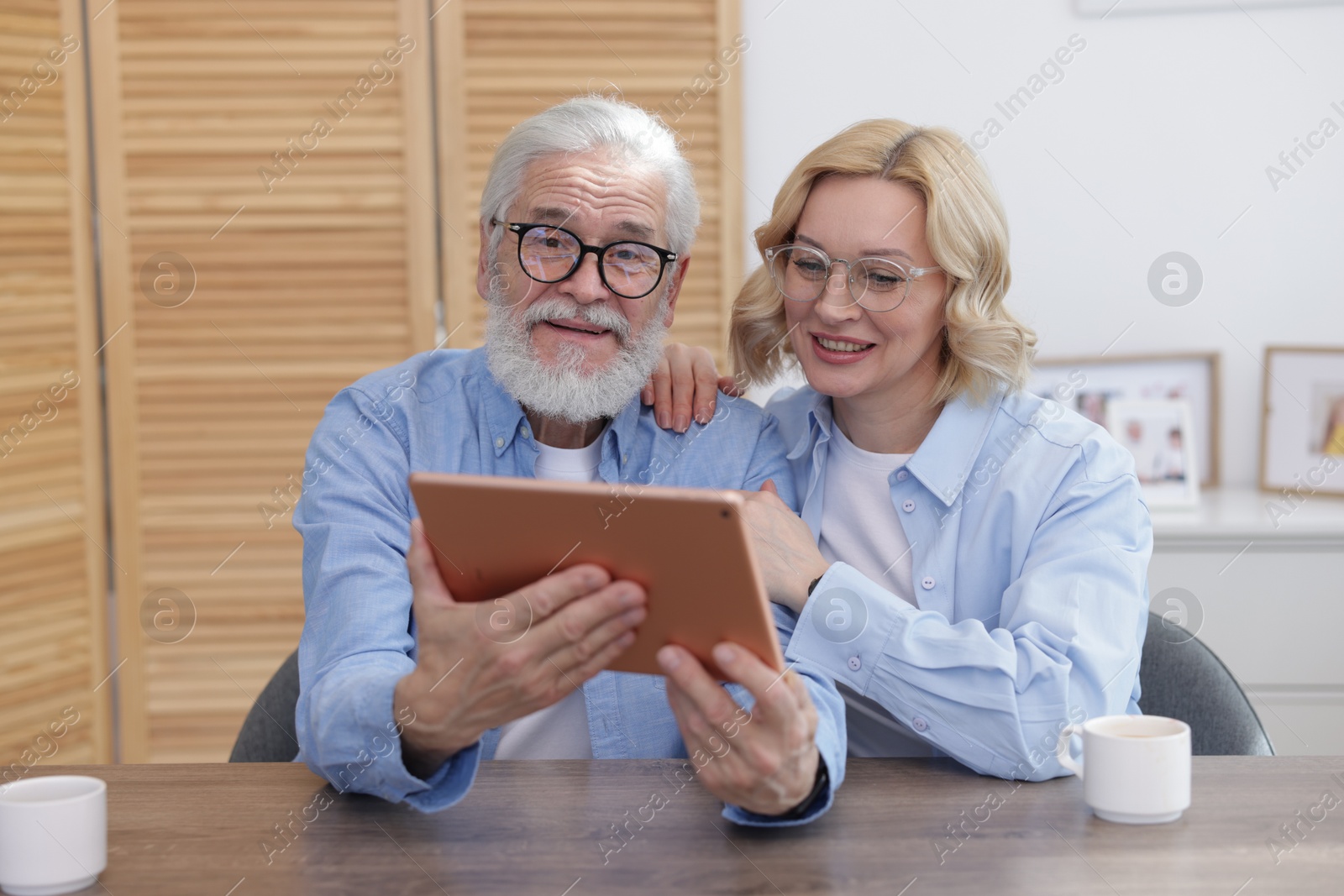 Photo of Senior man and mature woman watching something on tablet at home. Happy couple