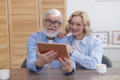 Senior man and mature woman watching something on tablet at home. Happy couple