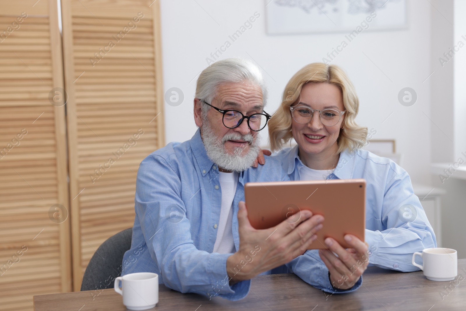 Photo of Senior man and mature woman watching something on tablet at home. Happy couple